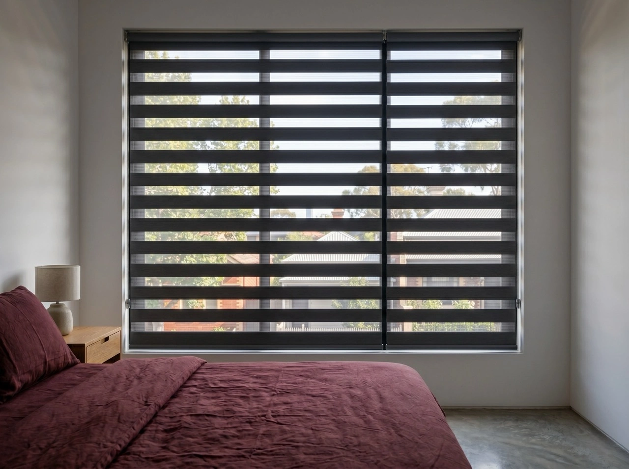 Blockout zebra blinds Melbourne in a minimalist bedroom with charcoal bands, burgundy bedding and bedside lamp
