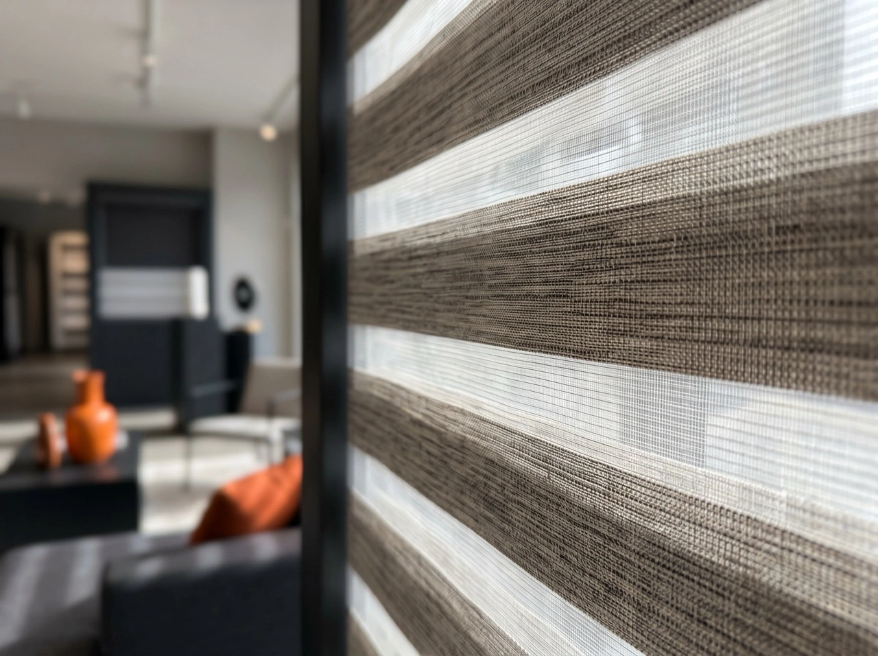 Custom texture zebra blinds Melbourne with woven fabric stripes in a contemporary living room with charcoal sofa and orange accents