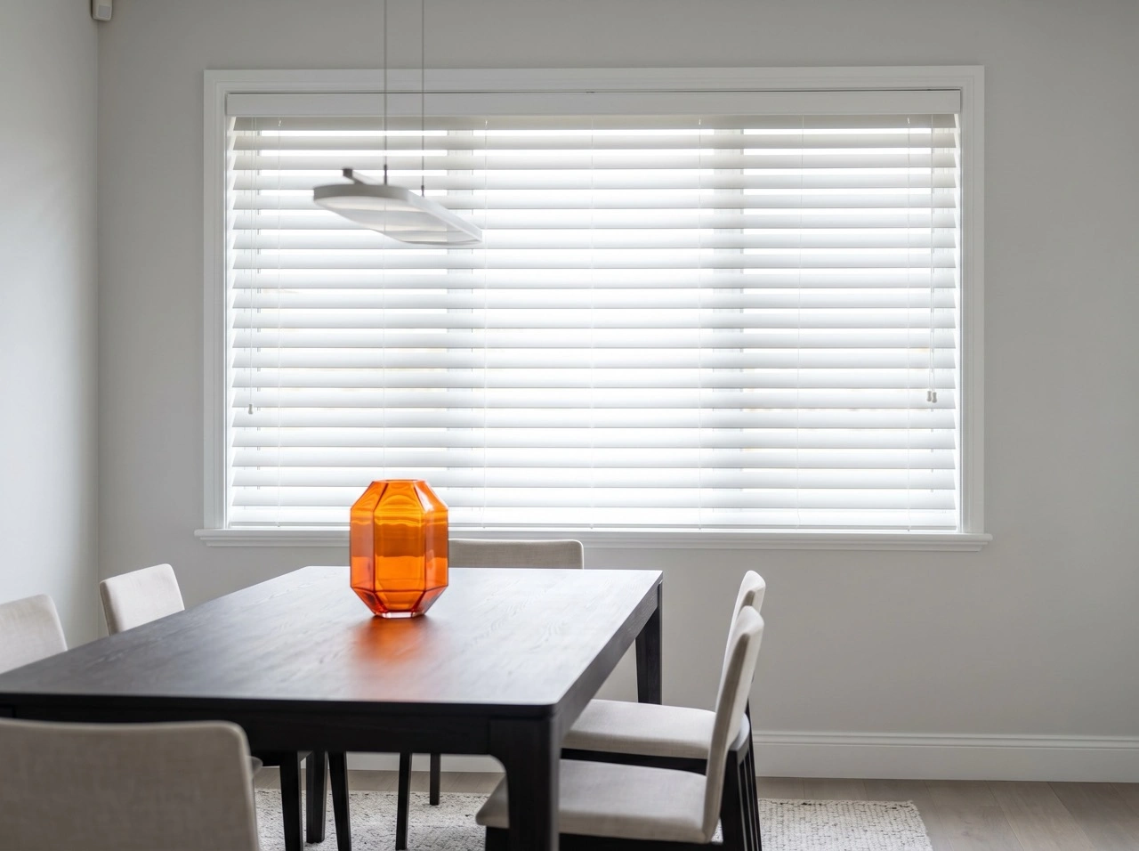 White venetian blinds Melbourne in a bright dining room with dark timber table, white chairs and amber glass vase centerpiece