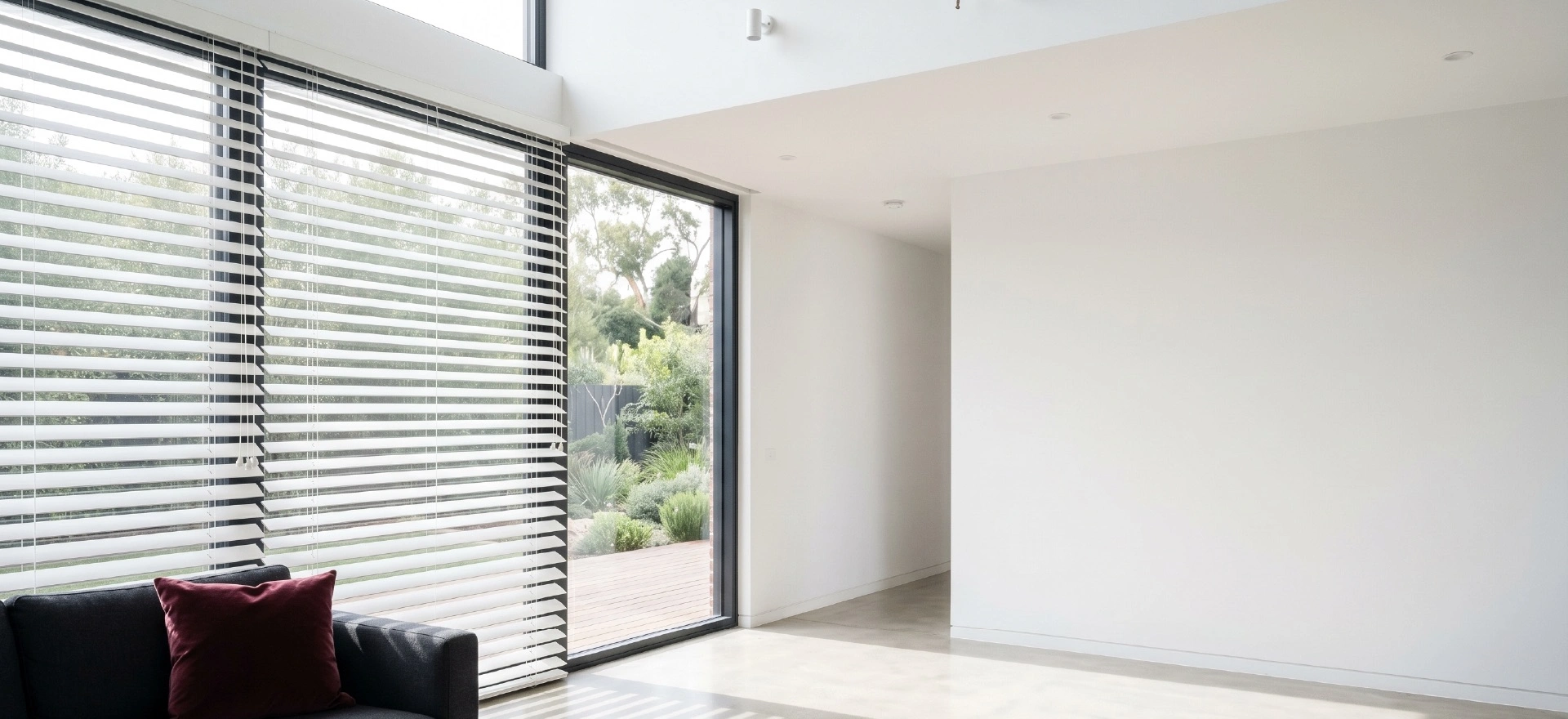 White venetian blinds Melbourne on large sliding glass doors in a spacious modern living area with garden views and charcoal sofa