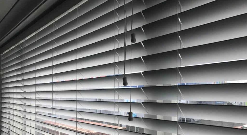 Venetian Blinds Melbourne: The Complete Buying Guide 5 Angled close-up of grey horizontal Venetian blind slats with suspended tilt control cords.