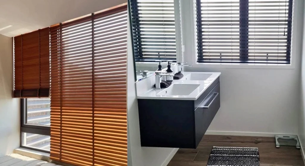 Venetian Blinds Melbourne: The Complete Buying Guide 4 Side-by-side comparison of warm wood-grain Venetian blinds on the left and black moisture-resistant bathroom Venetian blinds on the right above a vanity.