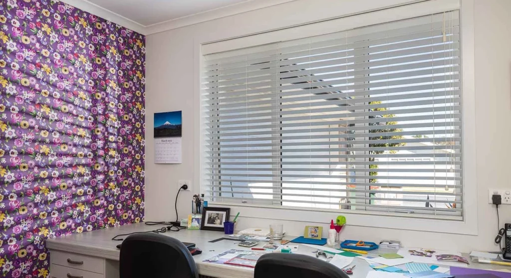 Venetian Blinds Melbourne: The Complete Buying Guide 6 White Venetian window blinds mounted above a home office desk and workspace beside a patterned feature wall.