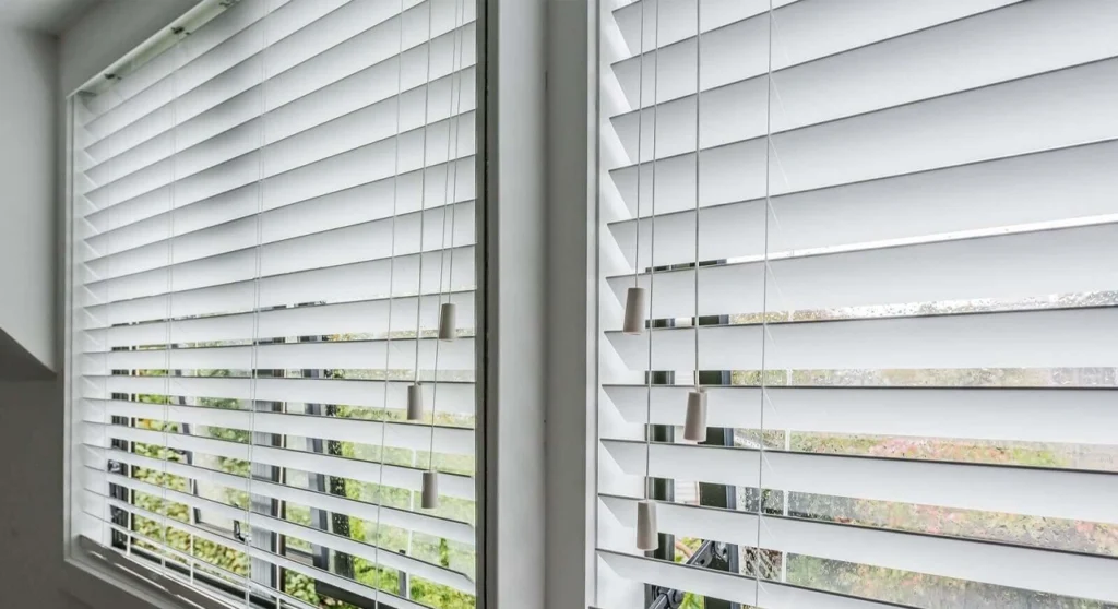 Venetian Blinds Melbourne: The Complete Buying Guide 3 Close-up of white horizontal Venetian blind slats showing vertical ladder cords and hanging control tassels against a window.